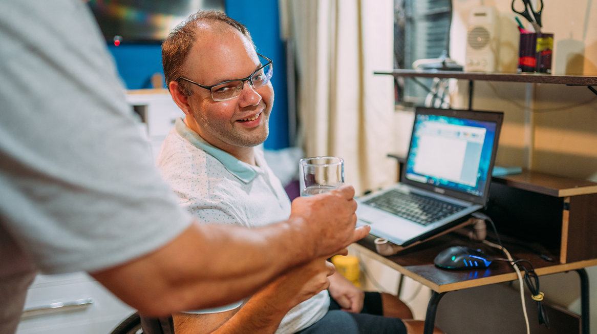 Man with an IDD using a laptop, being handed a glass of water.